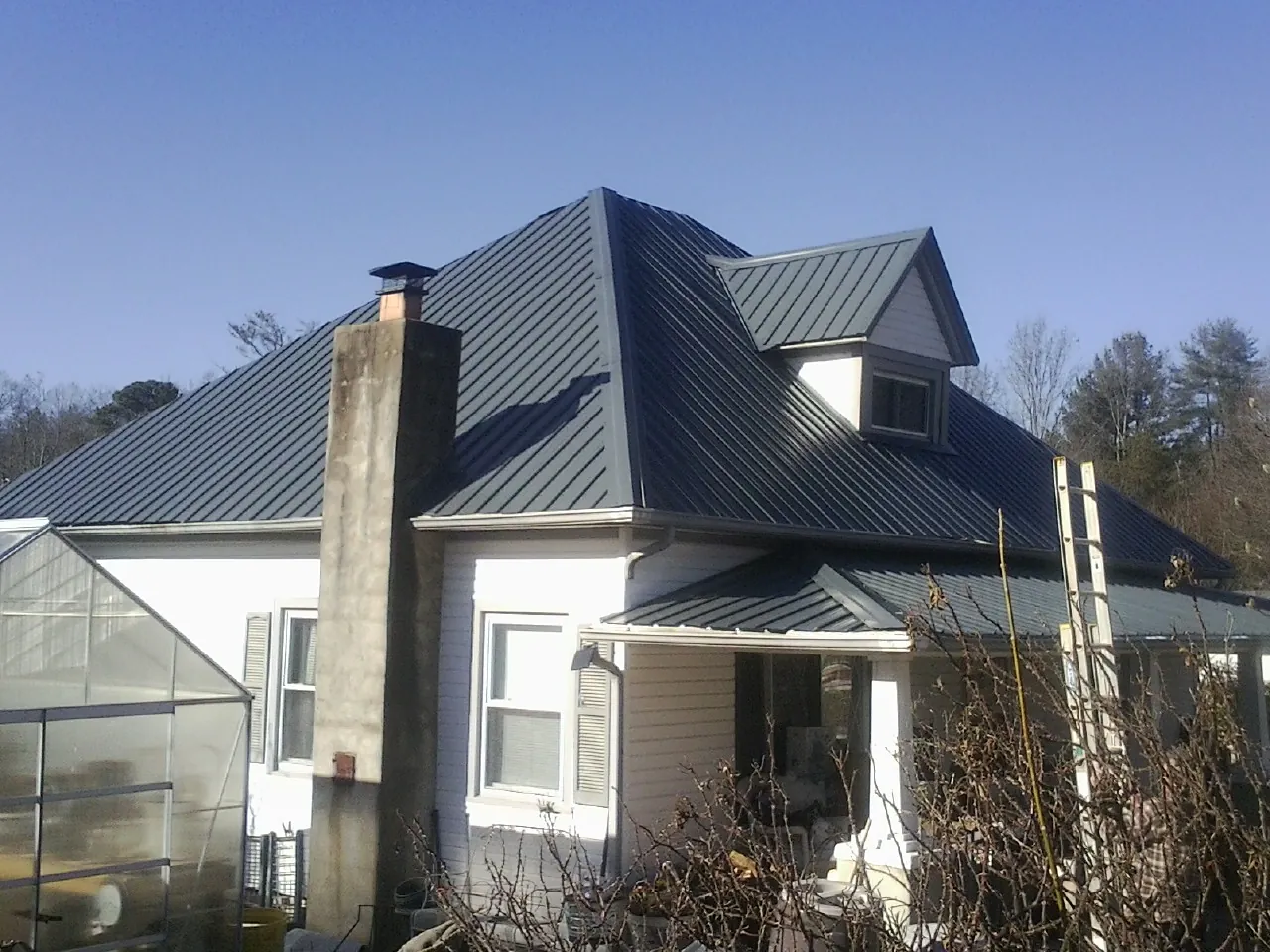 Dark blue standing seam metal roof on a white farmhouse with dormer — Slate & Tile Roof Repair by Roofing Brothers in Milford Center