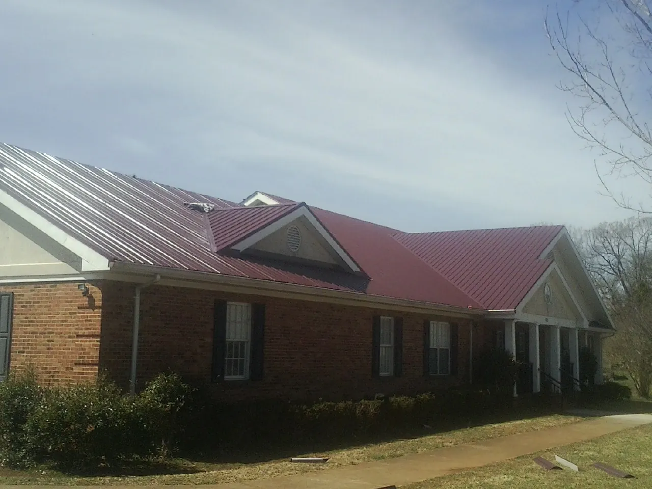Red metal roof with gabled entries on a long brick building, from a Hail Damage Roof Repair job in Milford Center