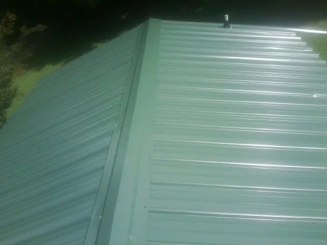 New green metal panels meeting at the ridge of a roof — Flat Roof Repair work by our crew in Milford Center