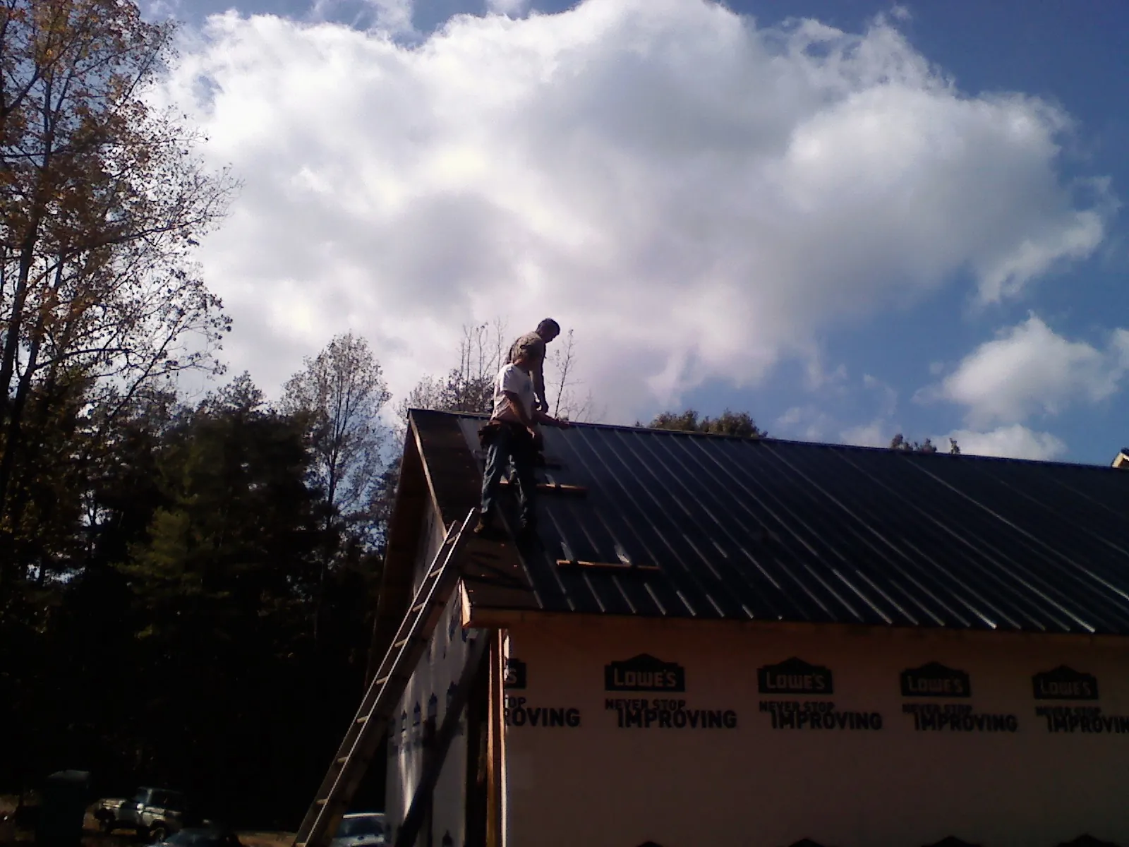 Roofer fastening dark metal panels high against a cloudy sky, from a Roof Inspection job in Milford Center
