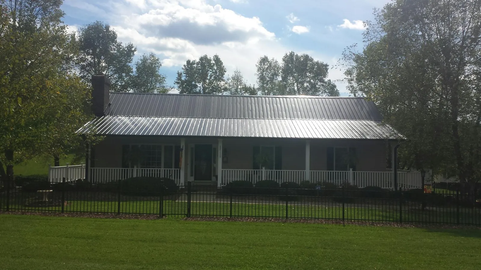 Gray metal roof on a brick ranch with a full width front porch — Gutter Guard Installation work by our crew in Milford Center