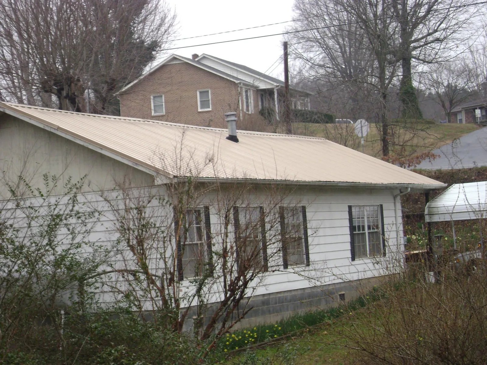 Tan metal roof on a white sided house set into a hillside — Commercial Roofing by Roofing Brothers in Milford Center