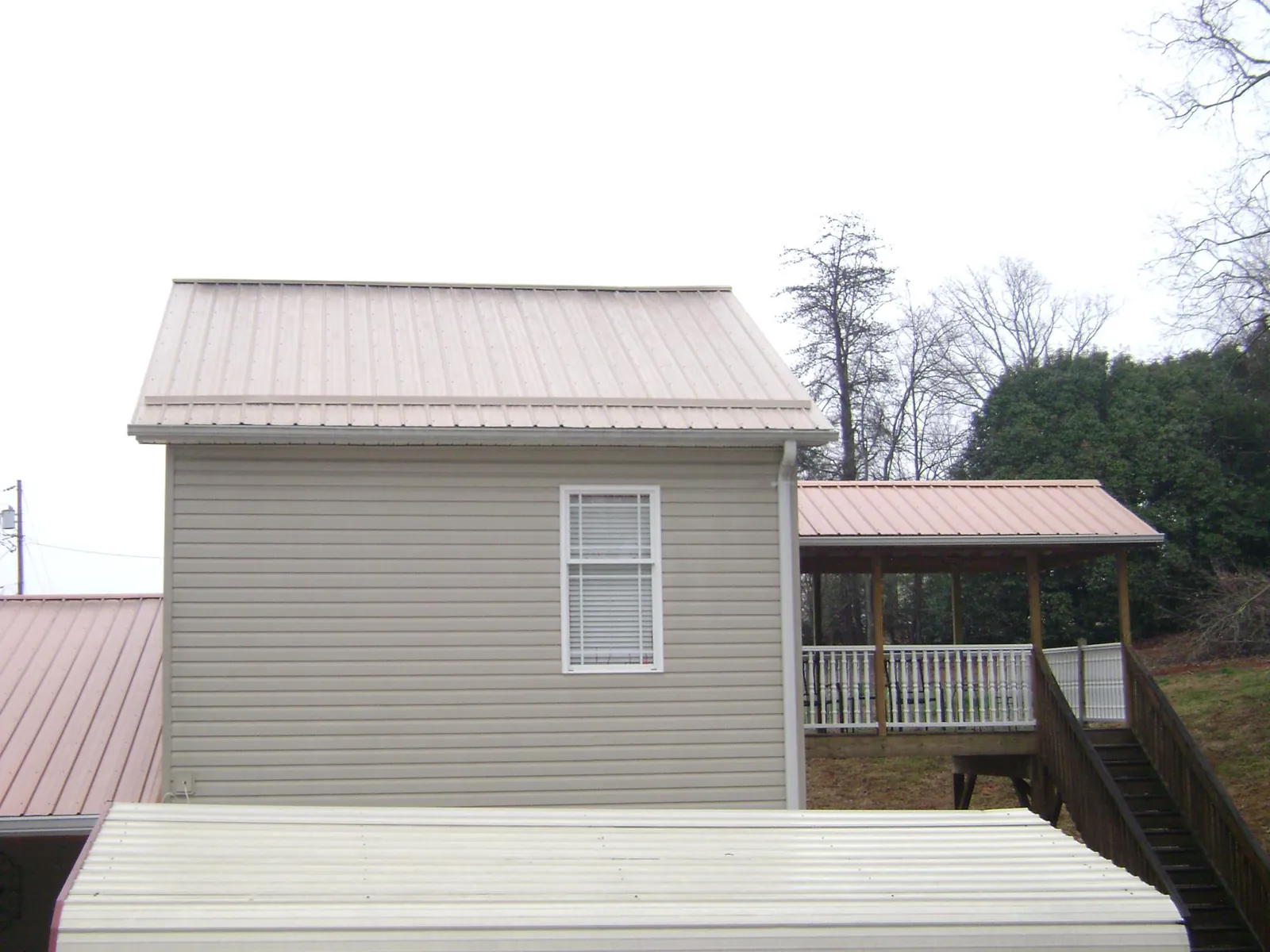 Tan metal roofs on a two story addition and attached porch, from a Roof Replacement job in Milford Center